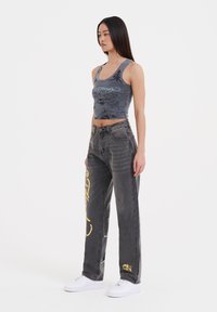 Gray cropped tank top with dragon graphic paired with gray denim jeans featuring yellow accents and white sneakers.