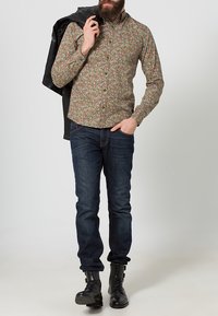 Bloemmotief shirt in groen, rood en wit, gemaakt van katoen. Slim-fit donkerblauwe jeans en zwarte laarzen. Jas over de schouder.