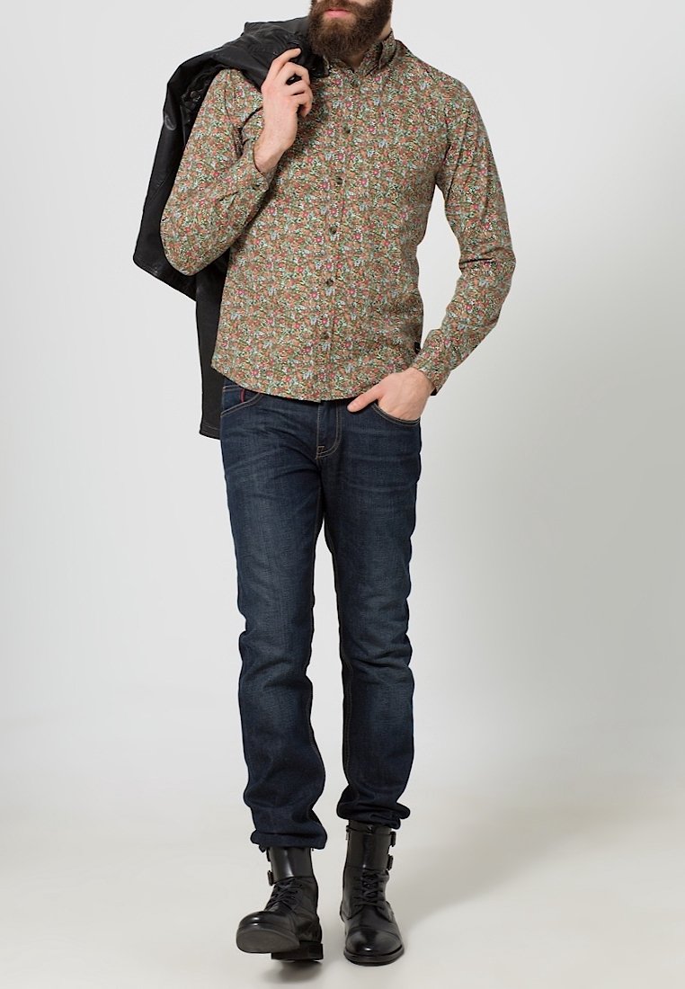 Bloemmotief shirt in groen, rood en wit, gemaakt van katoen. Slim-fit donkerblauwe jeans en zwarte laarzen. Jas over de schouder.