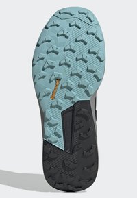 Semelle de chaussure noire et bleu clair avec un motif de grip en caoutchouc texturé, présentant un logo orange et une structure stabilisante intégrée.