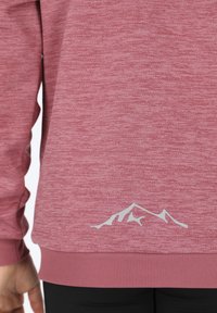 Ljusrosa fleece-tröja med strukturerad yta, ribbad nederdel och en subtil vit bergsgrafik på nedre delen av ryggen.