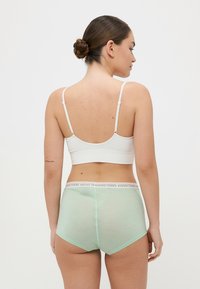 Bela rebrasta bralette in svetlo zelene hlačke s logotipom na pasu. Mehka, elastična tkanina, ki ima gladko teksturo in subtilen dizajn.