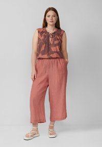 Top sans manches à motif rouille avec un col froncé, associé à un pantalon large plissé en rouille uni, complété par des sandales blanches à lanières.