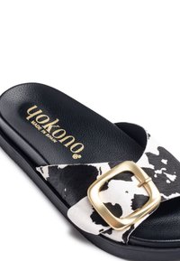 Slide sandal with black synthetic sole, cow print upper, and a gold buckle accent. Textured footbed with brand logo embossed in gold.