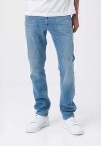 Jeans in denim azzurro chiaro con una vestibilità dritta, caratterizzati da distintive tasche frontali e una leggera scoloritura. Abbinati a sneaker bianche.