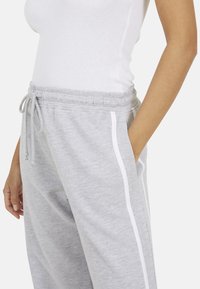Grijze sweatpants met een elastische tailleband, zijzakken en witte strepen aan de zijkanten. Zacht materiaal en een losse pasvorm.