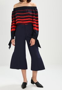 Blusa rossa e blu a righe con scollo off-the-shoulder e maniche lunghe, abbinata a pantaloni cropped larghi blu navy. Vestibilità slim, tessuto testurizzato, lunghezza alla caviglia.