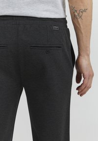 Dark gray sweatpants with a smooth texture, featuring a drawstring waist, side pockets, and a small tag on the back.
