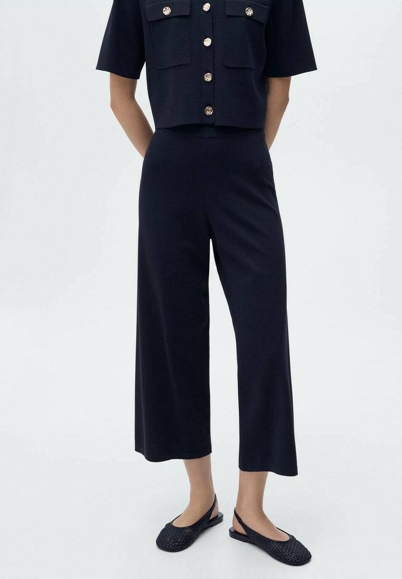 Haut court marine à manches courtes, boutons dorés et deux poches avant. Assorti avec un pantalon large marine et des chaussures à enfiler noires en tressé.