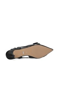 Zapato negro de tacón alto con punta afilada, con laterales recortados y parte superior de cuero liso. La suela es beige con textura mínima para agarre.