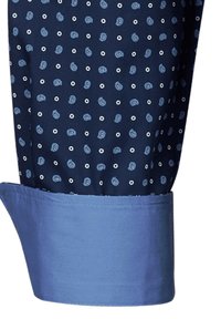 Manica di camicia blu navy con un piccolo motivo a pois in azzurro chiaro e bianco, caratterizzata da un polsino blu uniforme con una texture liscia.