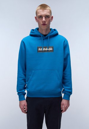 Blue cotton hoodie with a front kangaroo pocket, drawstring hood, and a black rectangular logo patch at the chest. Smooth texture, relaxed fit.