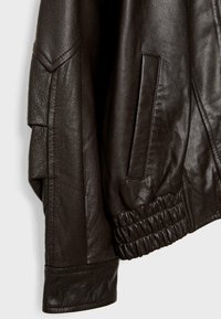 Giubbotto in pelle marrone caratterizzato da materiale testurizzato, vita elastica e tasche laterali; ha un design strutturato con cuciture distintive.