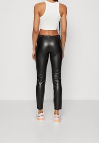 Pantalons taille haute en simili cuir noir avec des jambes fuselées, une texture lisse et une taille élastique, associés à des baskets blanches.