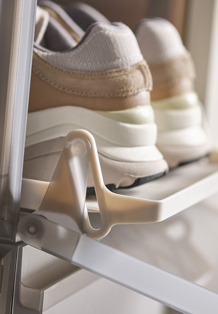 Sneaker mit einer Farbgebung in Beige, Grau und Weiß stehen auf einem klaren Kunststoffregal, das eine gebogene, weiße Kunststoffstütze aufweist.