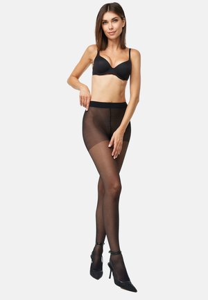 Collants noirs transparents avec une texture lisse et une taille haute, assortis à des talons hauts noirs et un soutien-gorge noir sur un fond neutre.