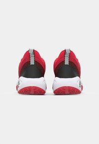 Red athletic shoes featuring a mesh upper, padded collar, black accents, and a white outsole with red detailing. Textured heel counter included.