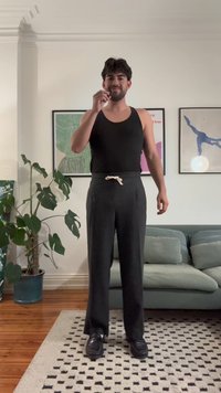 Camiseta preta sem mangas e calças cinza escuro com cintura elástica. As calças têm um corte solto. Tecido suave, usadas com sapatos pretos.
