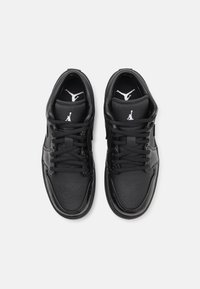 Zapatos deportivos negros con parte superior de cuero texturizado, acentos de malla y cordones negros. Presenta un logo en la lengüeta y una suela de goma lisa.