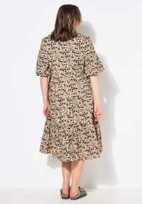 Bloemenjurk met korte pofmouwen, beige basis, zwarte bloemenpatronen en een tiered zoom tot op de knie. Lichtgewicht stof en een ontspannen pasvorm.