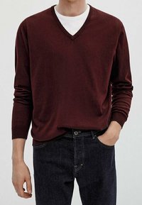 Bordeaux gebreide trui met een V-hals, lange mouwen en een relaxte pasvorm, gedragen over een wit T-shirt, in combinatie met donkere denim jeans.