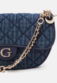 Prošívaná džínová crossbody taška v tmavě modré barvě s zlatým řetězovým popruhem a akcentem. Obsahuje výrazné G logo na klopě a dekorační přívěsek.