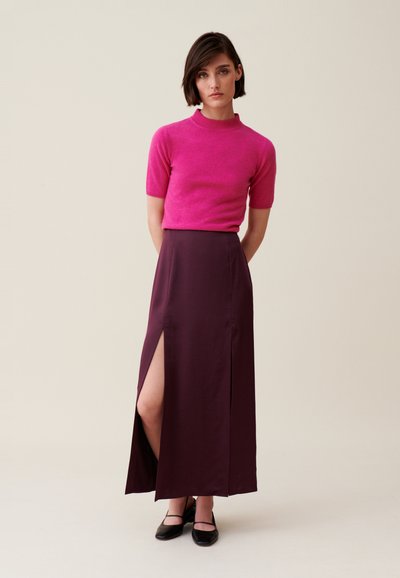 Maglione fucsia a maglia con maniche corte, abbinato a una gonna lunga bordeaux con uno spacco laterale. Ballerine nere completano l'outfit.