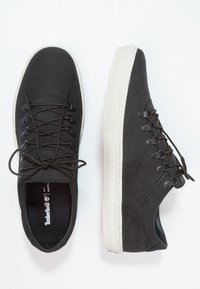 Les baskets en cuir noir présentent un bout rond, un design à lacets avec des lacets brun foncé, et une semelle en caoutchouc blanche contrastée avec des détails de couture.