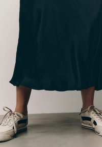 Gonna midi nera in satin con una texture liscia che si allarga all'orlo; abbinata a sneakers beige con accenti neri e lacci beige.