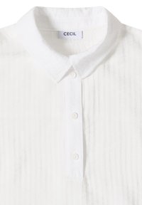 Chemise blanche texturée à boutons avec col classique et trois boutons visibles sur la patte de boutonnage avant.