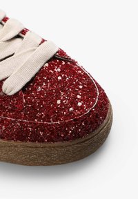 Røde glitrende sneakers med en tekstureret overflade, cremede snørebånd og en brun gummisål. Har et afrundet tådesign og glitrende accenter.