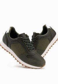 Zielone buty sportowe z teksturowanymi panelami z tkaniny, gładkimi skórzanymi detalami, białym obcasem i brązową gumową podeszwą. Posiadają sznurowane zapięcie.