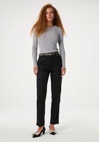 Grijze geribbelde top met lange mouwen en versieringen, gecombineerd met zwarte pantalon met streepjes en zwarte hakken met zilveren strikaccenten.
