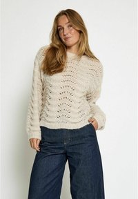 Knit sweater in light beige featuring a textured pattern and wide cuffs, paired with dark blue wide-leg pants.