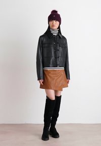 Veste en cuir noire avec deux poches sur le devant, col roulé rayé, mini-jupe en cuir marron et bottes noires jusqu'aux genoux. Bonnet en tricot violet avec pompon.