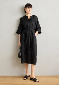 Μαύρο λινό midi φόρεμα με κολάρο, κουμπιά μπροστά, ζώνη στη μέση και τρία τέταρτα μανίκια. Συνοδεύεται από μαύρα σανδάλια slide.