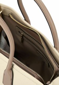 Bolso de mano de cuero beige con dos asas superiores, un compartimento con cremallera y un interior forrado. Detalles en hardware dorado a lo largo de la cremallera.
