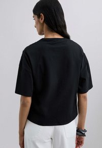 Camiseta negra de algodón con mangas cortas, corte relajado y escote redondeado. La parte posterior es lisa, sin patrones o acentos visibles.
