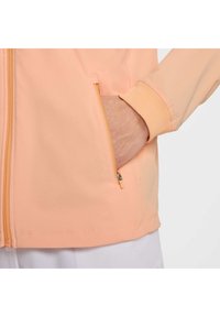 Chaqueta de melocotón claro con una textura suave, con cierre de cremallera y bolsillos para las manos. Puños y dobladillo acanalados para mayor comodidad.
