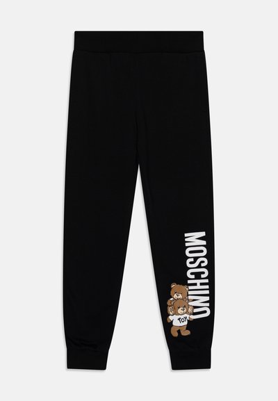 Sort joggerbukser lavet af blødt stof, med et bjørne-grafik og "MOSCHINO" tekst i hvid langs siden. Elastisk talje, tapered manchetter.