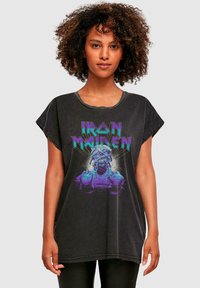 Musta ylisuurennettu t-paita lyhyillä hihoilla, jossa on kirkas violetti ja vihreä Iron Maiden -kuvio luurangosta.