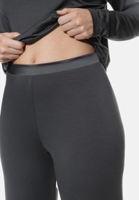 Donkergrijze legging met een gladde textuur en een naadloze tailleband, gedragen met een bijpassend langmouwtop, waarbij het middenrif zichtbaar is.