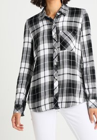 Black and white plaid button-up shirt with a collar, long sleeves, a chest pocket, and a relaxed fit. Soft fabric with a checkered pattern.