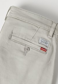 Pantalon Levi’s beige clair montrant une poche arrière avec fermeture à bouton et deux étiquettes de marque Levi’s cousues au-dessus.