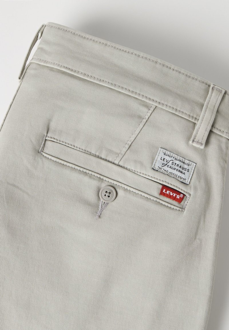 Pantalon Levi’s beige clair montrant une poche arrière avec fermeture à bouton et deux étiquettes de marque Levi’s cousues au-dessus.
