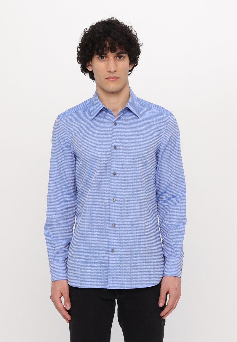 Camisa de manga larga azul con un patrón texturizado y rayas horizontales blancas, que presenta un cuello abotonado y botones grises.
