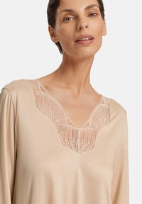 Blusa beige con scollatura a V e dettagli in pizzo intricati sul collo. Maniche lunghe in una texture di tessuto liscia.