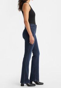 Jeans svasati blu scuro in denim, con vita a media altezza e un classico design a cinque tasche. Indossati con un top nero senza maniche.