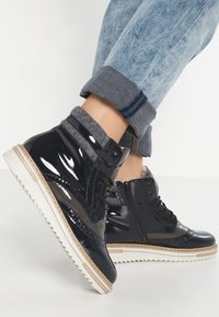 Svart lackläder ankelstövlar med grått tygkant, sidoglägga, snören och beige gummisulor, bärs med uppvikta ljusblå jeans.