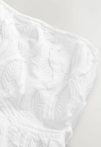 Bílá látka s texturovanými, vyšívanými vzory listů. Měkký, lehký materiál s detailními výšivkami podél okrajů.
